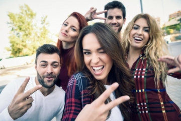 Group of friends taking selfie in urban background. Five young people wearing casual clothes.