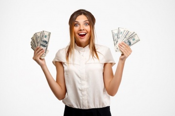 Portrait of young successful businesswoman smiling, surprised, looking at camera, holding money over white background.