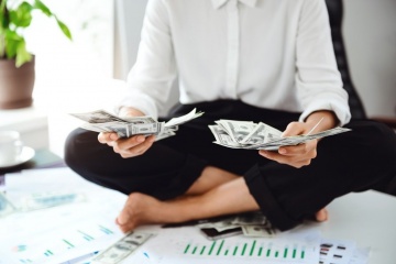 Young beautiful businesswoman holding money, sitting on table at workplace in office. Close up.