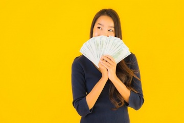 Portrait beautiful young asian woman with money and cash on yellow isolated background