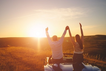 Leisure road trip travel and people concept happy man couple driving in cabriolet car at country enjoying sunset holding hands up